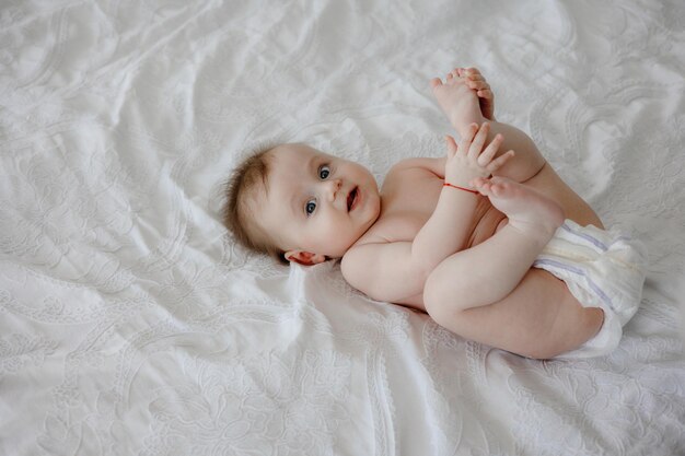 A baby with blue eyes is laying on a bed with a white sheet.