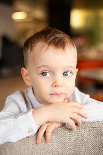 a baby with blue eyes and a striped shirt is sitting on a couch