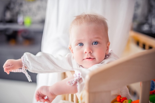 Baby with a cute happy face is standing in a cot and smilingfunny childrenhappy family