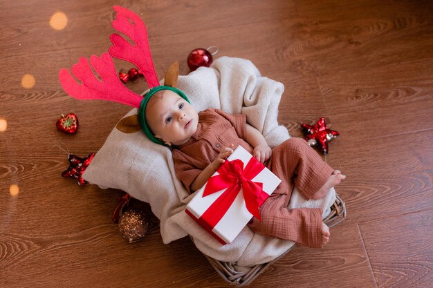 Baby with deer horns on his head lies on gray linen blanket in a wicker basket. Christmas, new year. Christmas present. Santa Claus' little helper. space for text. High quality photo