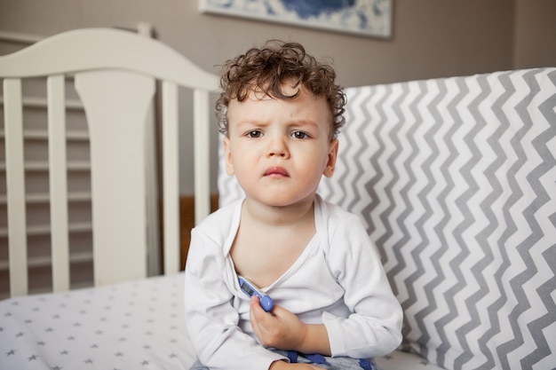 Baby with a fever. The boy is a small child with a thermometer under his arm sitting on the bed. Sick, sad.