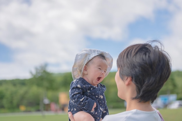 A baby with a hat on is yawning in a park.