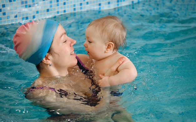 Baby with mother trainer in indoor swimming pool having lesson