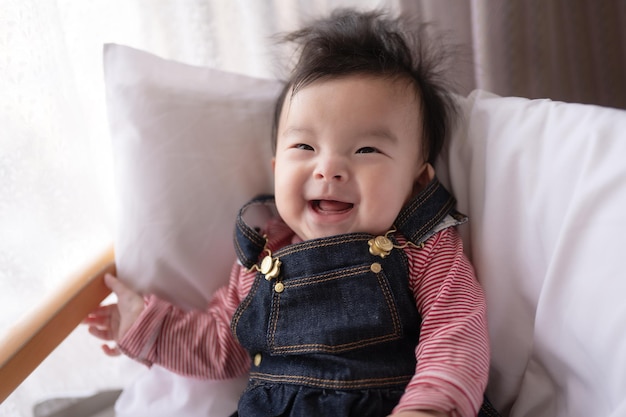 A baby with a pink striped shirt and denim overalls smiles at the camera.