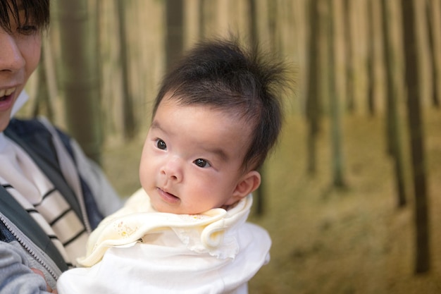 A baby with a yellow scarf is being carried by a woman.