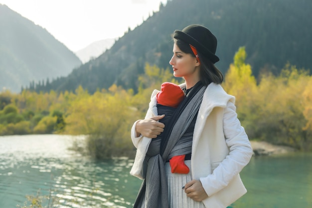 Babywearing Mother is carrying her child and travel in autumn mountain lake