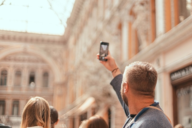 Back close up view of a young man takes pictures of the architecture of a building or landmarks on h...