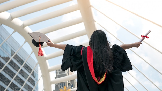 Back of girl in black gowns and hold diploma certificate with happy graduated.