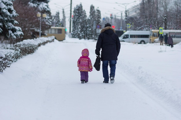 Back of man and child going away in snowy park in winter