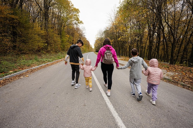 Back of mother with four kids running on road at autumn fall forest