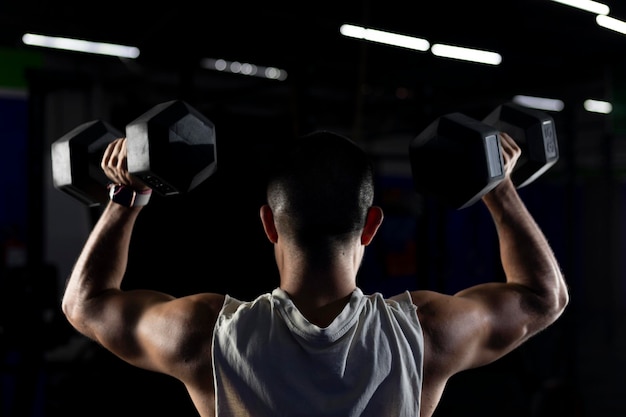 Back of a muscular man doing exercises with dumbbells in the gym