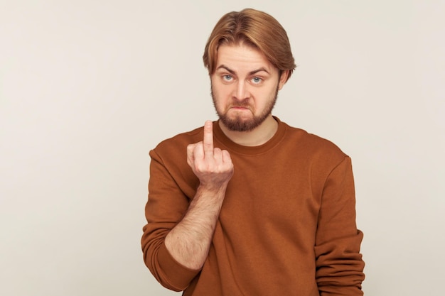 Back off Portrait of irritated bearded man in sweatshirt looking with hate disrespect showing middle finger