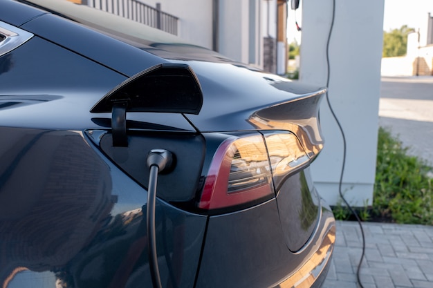 Back part of black electric car with plugged charging cable