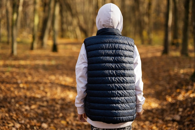 Back portrait of teen boy in hoodie and sleeveless vest at fall forest