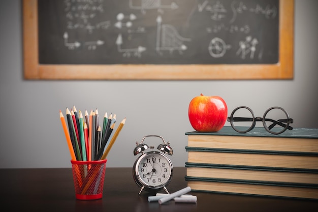 Back to school background with books pencils and apple over chalkboard and wooden table