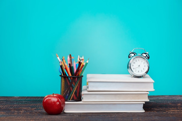 Back to School concept. Books, colored pencils and clock on blue wall