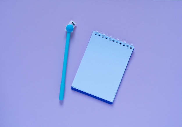 Back to school concept. Notepad and blue pen on a pink background. View from above. Flat lay with copy space.