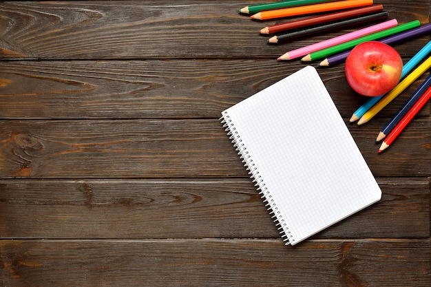 Back to school concept. Open notebook and apple with colored pencils on wooden background