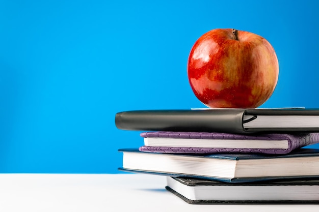 Back to school concept A stack of books and an apple on blue background Place for text