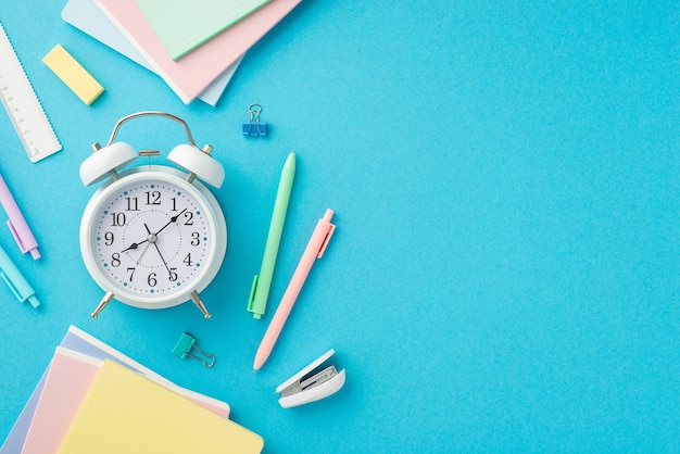 Back to school concept Top view photo of colorful stationery alarm clock notepads pens binder clips mini stapler ruler and eraser on isolated blue background with copyspace