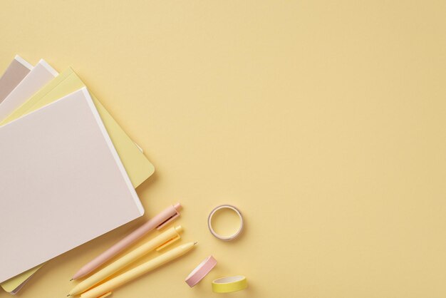 Photo back to school concept top view photo of school supplies diaries adhesive tape and pens on isolated pastel yellow background with copyspace