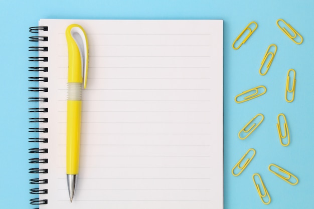 Back to school creative . Notepad with yellow pen and clips on a blue background.