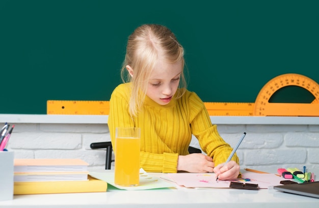 Back to school cute pupil girl drawing at the desk child in the class room with blackboard on