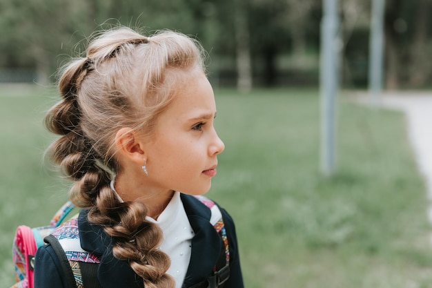 Back to school face portrait little happy kid pupil schoolgirl eight years old in fashion uniform with backpack and hairstyle voluminous long braid ready going second grade first day primary school