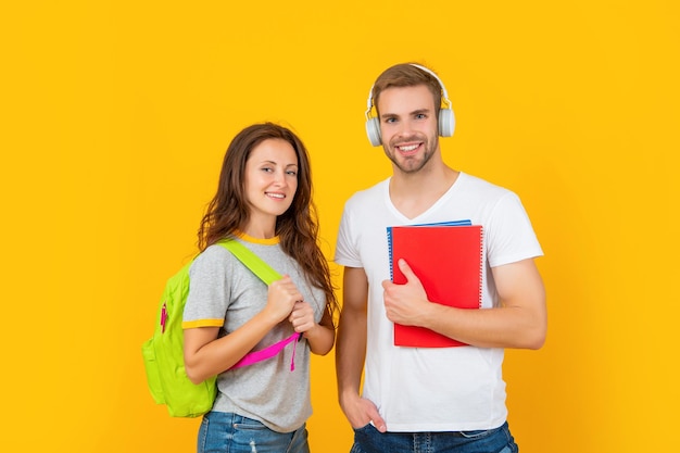 Back to school. modern education. knowledge day. guy and girl hold notebook. university students on yellow background. study with workbook. smiling couple in headphones and backpack.