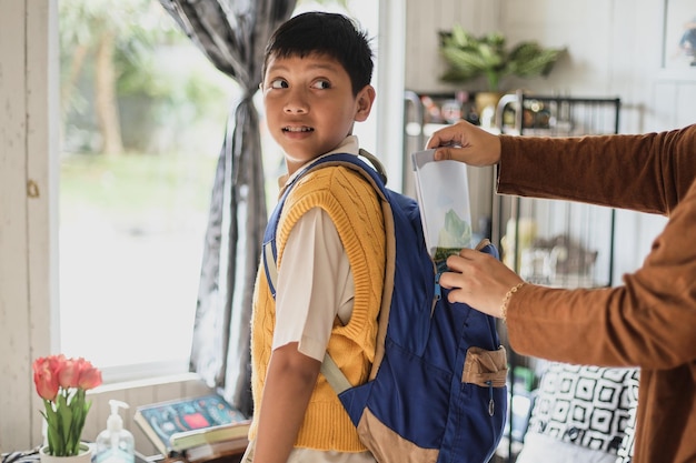 Back to school. Mother inserting books into the bag of her happy son during the preparing for school