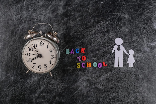 Back to school. Paper father with daughter on chalk blackboard with text back to school and alarm clock