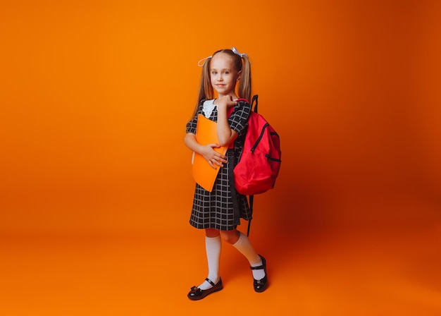 Back to school A schoolgirl with a school bag on an isolated yellow studio background a little girl holds a folder and a backpack