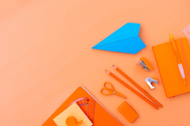 Back to school styled border with school supplies and paper plane on orange background with copy space