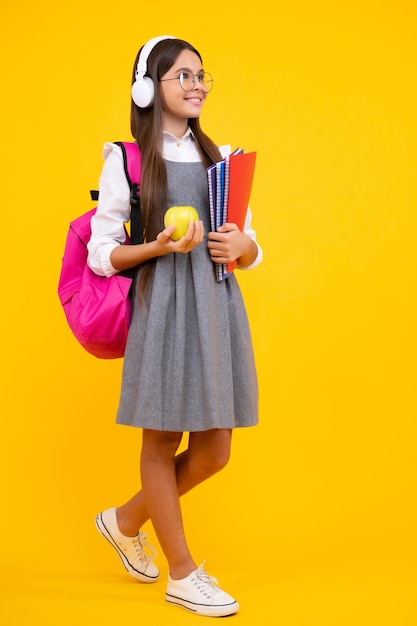 Back to school Teenage school girl with bag hold apple and book ready to learn School child on isolated yellow studio background Happy face positive and smiling emotions of teenager girl