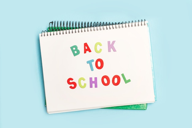 Back to school write in a notebook with colored toy wooden letters on a light blue background