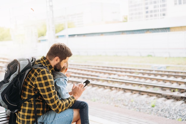 Back shot of caucasian man holding children hands walking along platform going to take train