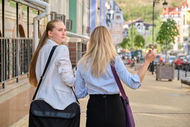 Back shot of two young business women walking and talking in the city, female office employees