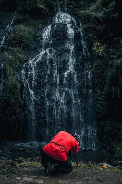 Back side of photographer in red tshirt with modern camera photography capturing waterfall landscap