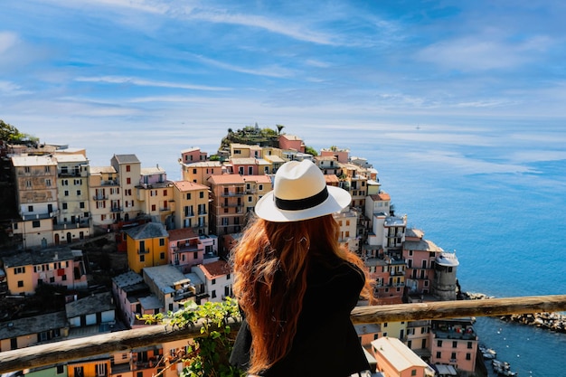 Back side of young stylish woman looking at panoramic view of Riomaggiore colorful village Cinque Terre Italy