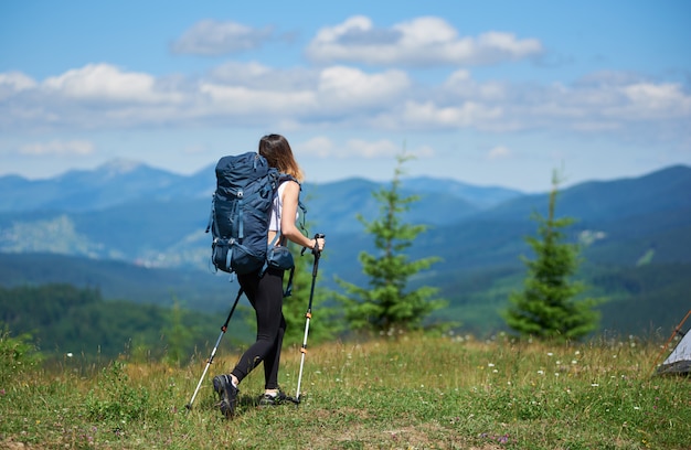 Back view of active female traveller with backpack and trekking sticks