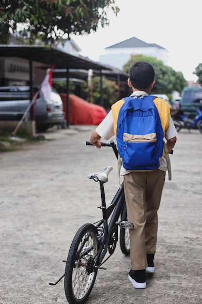 Back view of Asian boy wearing uniform and backpack going to school using bicycle.