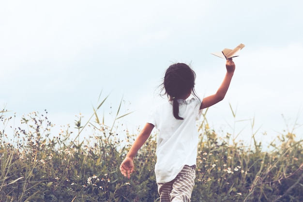 Back view of asian child playing toy paper airplane in the meadow in vintage color tone