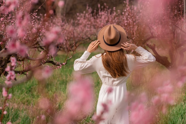 Back view of beautiful girl in a white blouse in the blooming garden, women's back, spring time