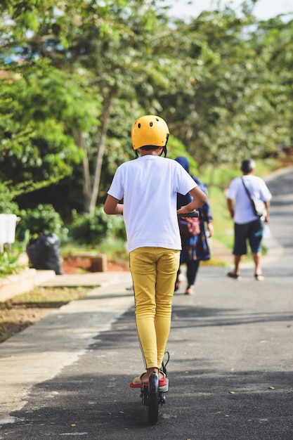 Back view of boy wear helmet enjoy having fun riding electric scooter at street park outdoors on sun