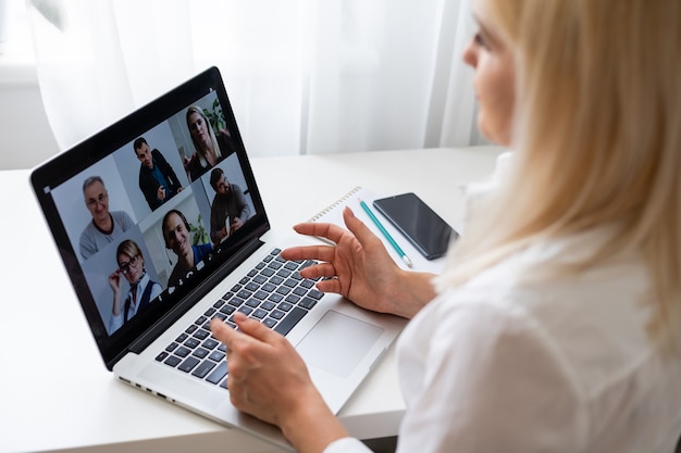 Back view of business woman talking to her colleagues about plan in video conference. Multiethnic business team using laptop for a online meeting in video call. Group of people smart working from home