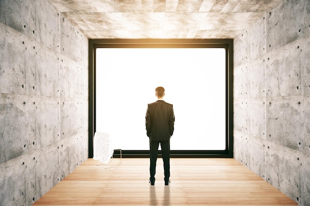 Back view of businessman in concrete interior looking out of window with no view Research concept 3D Rendering