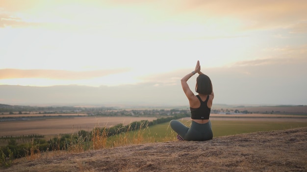 Back view of calm brunette woman meditating and sitting at lotus pose at the nature