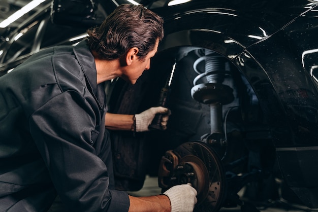 Back view of car mechanic sitting near the broken car in auto repair service at the car service garage. Automobiles concept