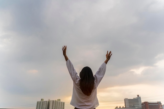 Back view of cheerful young asian woman with hands up raise Freedom concept