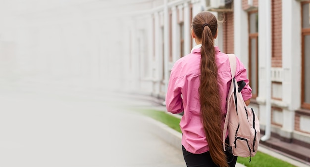 Back view of female student in pink shirt with backpack outdoors